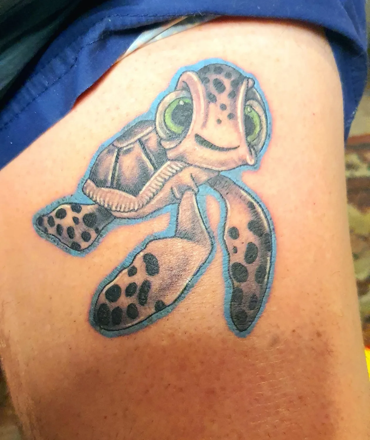 Colour tattoo of a smiling cartoon sea turtle outlined in blue